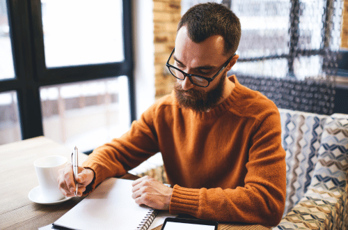 Man with glasses and a mustard jumper writing in a book