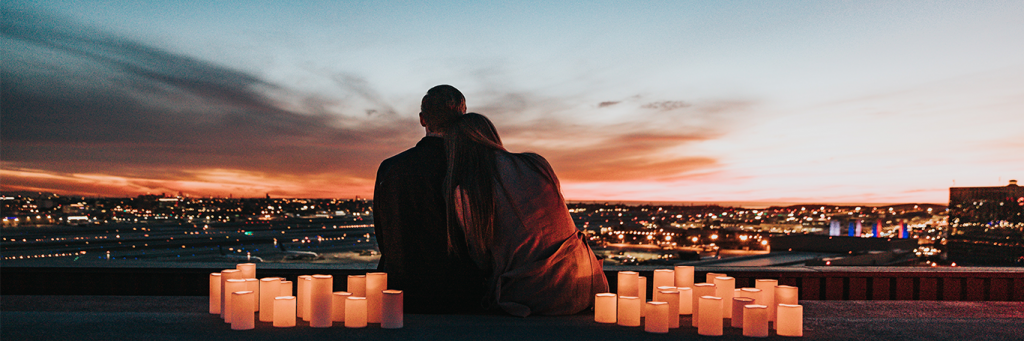 couple sits between candles watching vibration of city while girl lying head on boyfriend shoulder