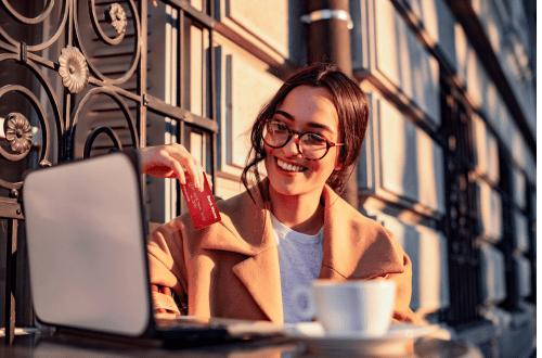 woman wearing glasses sitting in a cafe with a coffee with a debit card