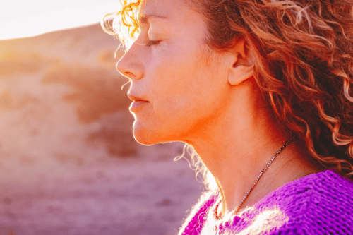 woman with pink jumper and blonde curly hair closing her eyes