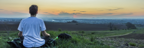 man sits on grass concentrates on meditation breathing in sunset sky