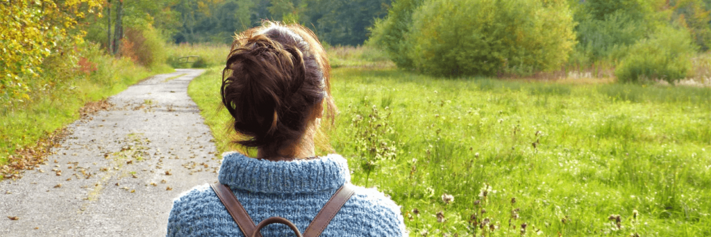 woman walks along footpath between green fields in beautiful weather