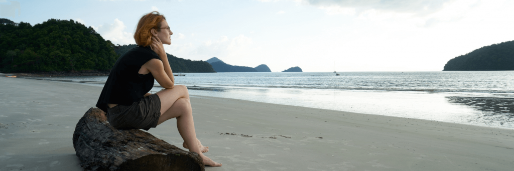 woman sits on tree on beach enjoying cool weather in cloudy sky