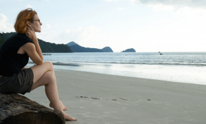 woman sits on tree on beach enjoying cool weather in cloudy sky