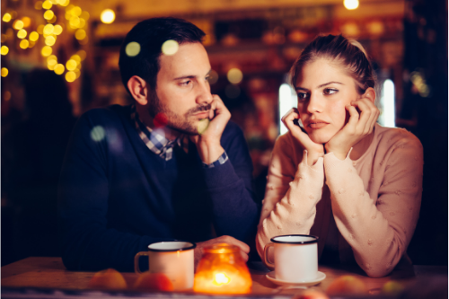 couple sitting at coffee shop with orange ambient candle looking frustrated