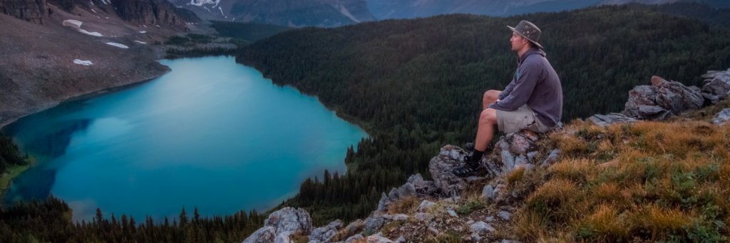 man sits on rock on top of mountain beside lake