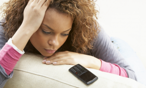 woman sadly sits on white couch looking at old model cellphone worrying