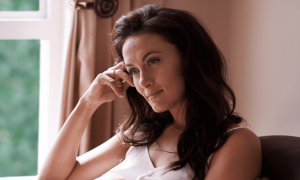 woman hand on face sit on couch beside window thinking