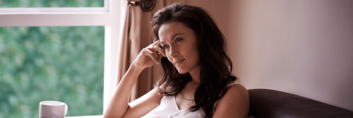 woman hand on face sit on couch beside window thinking