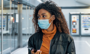 long curly brown hair woman wears face mask hand holding phone looks for store