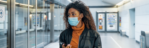 long curly brown hair woman wears face mask hand holding phone looks for store