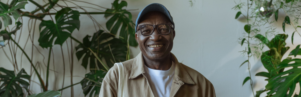 old man with black frame prescription glasses smiles plant pots behind