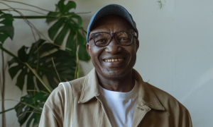 old man with black frame prescription glasses smiles plant pots behind