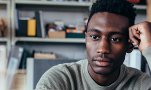 man hand on face sits alone in office room thinking