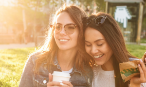 two girls smiles stands next to each other green field behind in beautiful sunny sky