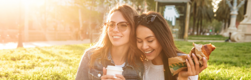 two girls smiles stands next to each other green field behind in beautiful sunny sky