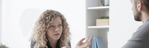 young woman with short curly blonde hair looks at man talking white drawer behind