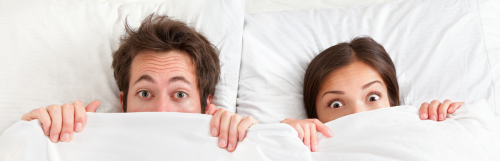 couple lies on white pillows starring covering face with big white blanket