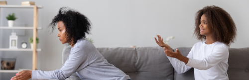 two curly hair women sit on grey couch argue in living room