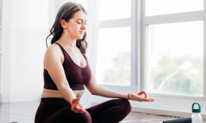 woman closes eyes focuses on breathing practicing meditation in peaceful living room