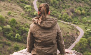 woman facing backward stands alone on rock sightseeing