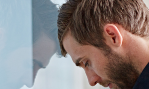 man stands head on glass feeling depressed sad exhausted tired