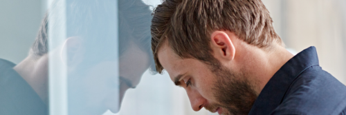 man stands head on glass feeling depressed sad exhausted tired