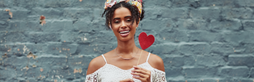 tanned skin girl happily smile carries red heart stick stands in blue stonewall background