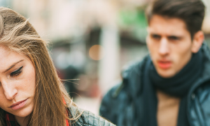 woman unhappily faces backward man hand up trying to explain