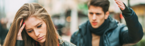 woman unhappily faces backward man hand up trying to explain