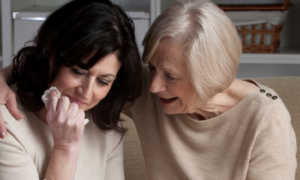 woman sits on couch in living room crying while elderly lady sitting beside comforting her