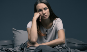 woman hand on face tiredly sits on bed lamps on experiences insomnia