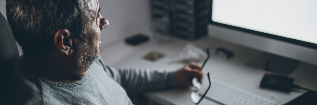 Worried senior man sitting in front computer, holding his glasses