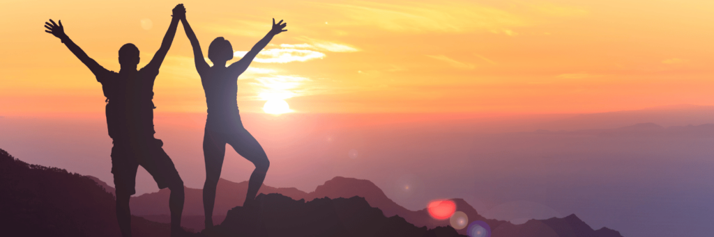 Two empowered people standing on a mountain looking at a golden sunset.