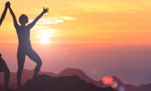 Two empowered people standing on a mountain looking at a golden sunset.