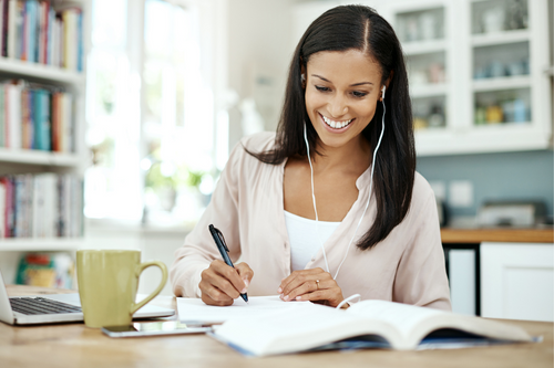 Shot of a young woman using a laptop and making notes at home