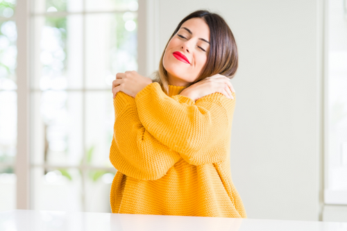 Young beautiful woman wearing winter sweater at home Hugging oneself happy and positive, smiling confident. Self love and self care